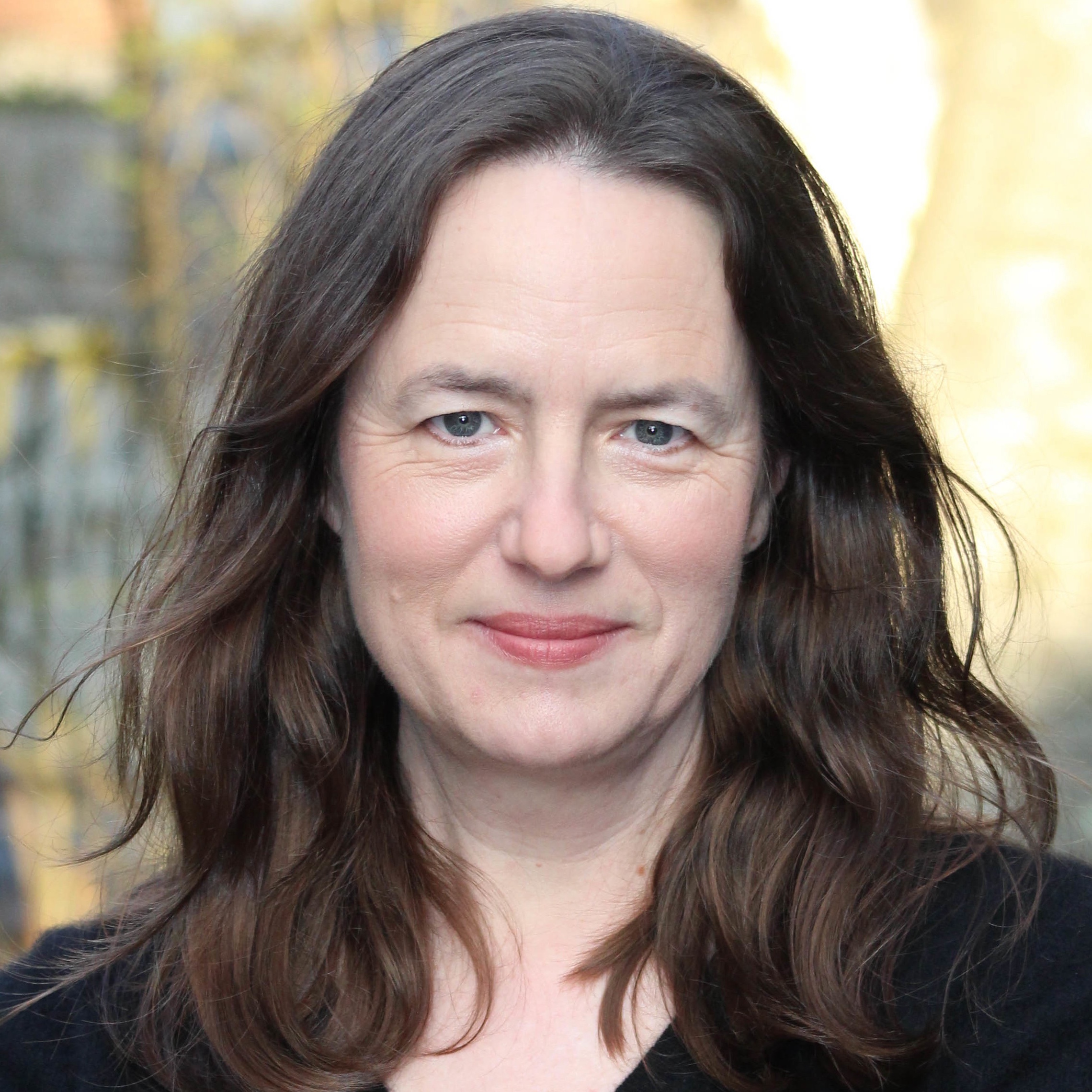 Portrait of the historian Heather Cox Richardson in purple top in front of a weathered building with cedar shakes.